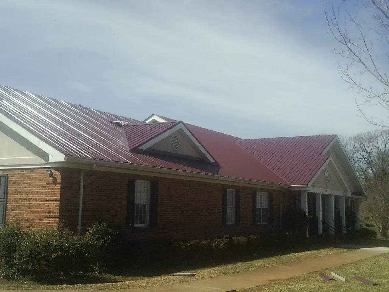 Red metal roof with gabled entries on a long brick building, from a Hail Damage Roof Repair job in Rotterdam Junction