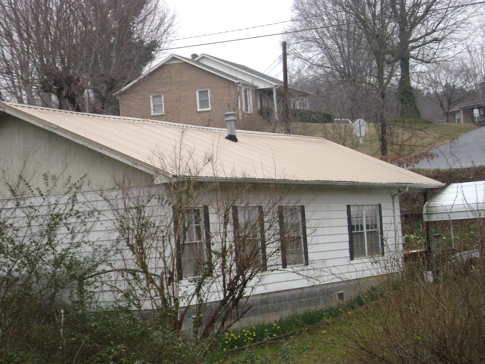 Tan metal roof on a white sided house set into a hillside — Commercial Roofing by Roofing Brothers in Rotterdam Junction